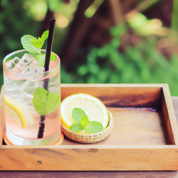 A glass of rose water lemonade garnished with mint and lemon slices on a rustic tray